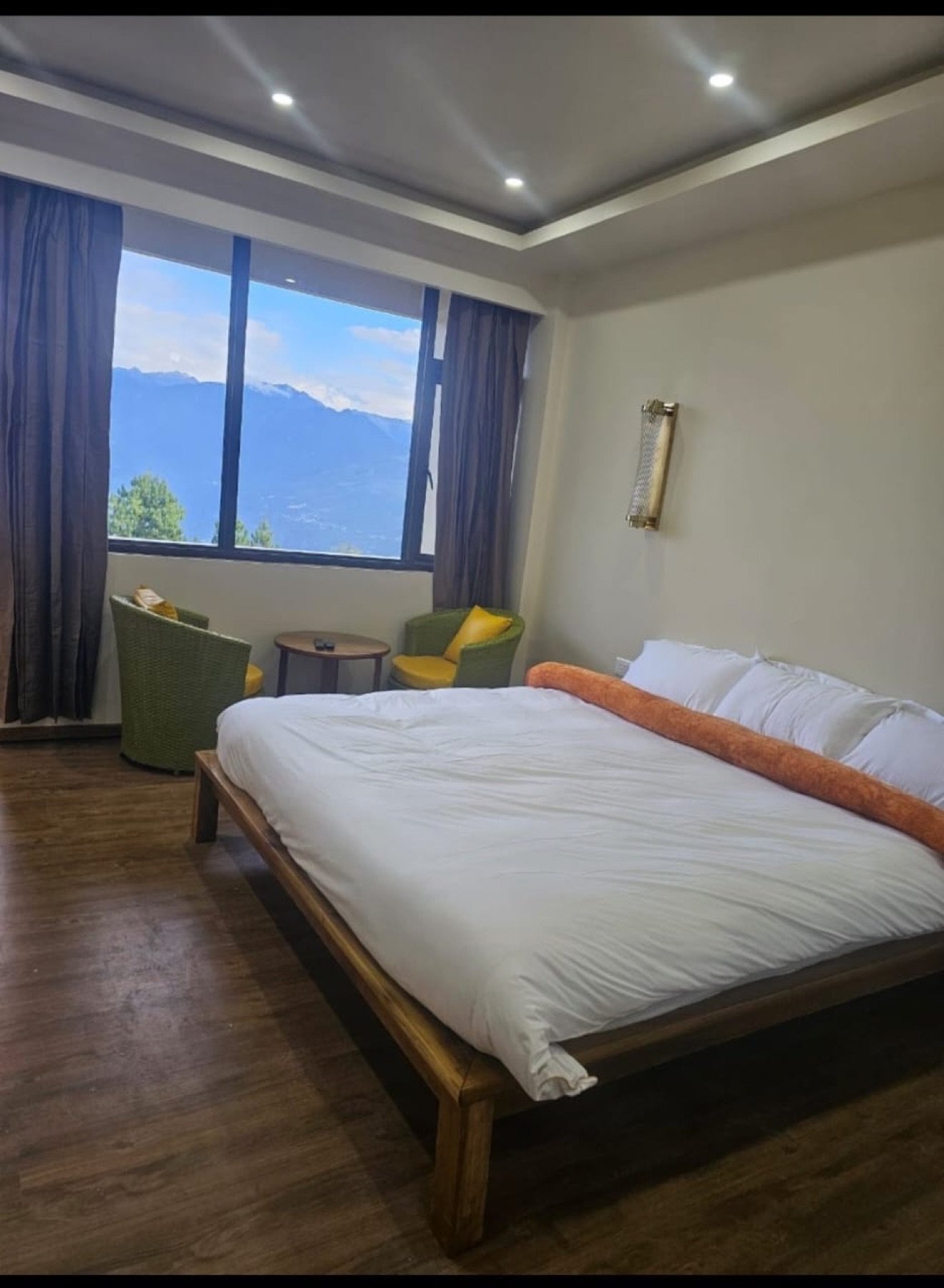 A Hotel Taktsang room with green wicker chairs and a wide window on snow-dusted peaks